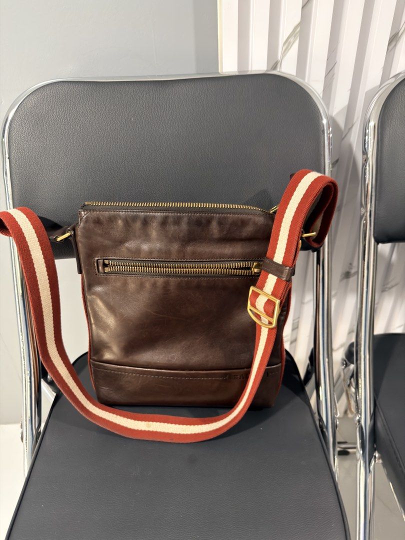 Bally Brown Leather Crossbody Bag (Category: Sling Bags) located in Quezon City. Submitted by houseoftrends_ (Listing ID 1466787090, Image 2). Description: Brown leather crossbody bag with distinctive red and white striped web strap. Gold-tone hardware throughout, including chunky double zippers on top and a zipped pocket on the front. Bally branding stamped on the leather and engraved on zipper pulls. Adjustable strap with metal buckle. Born in 