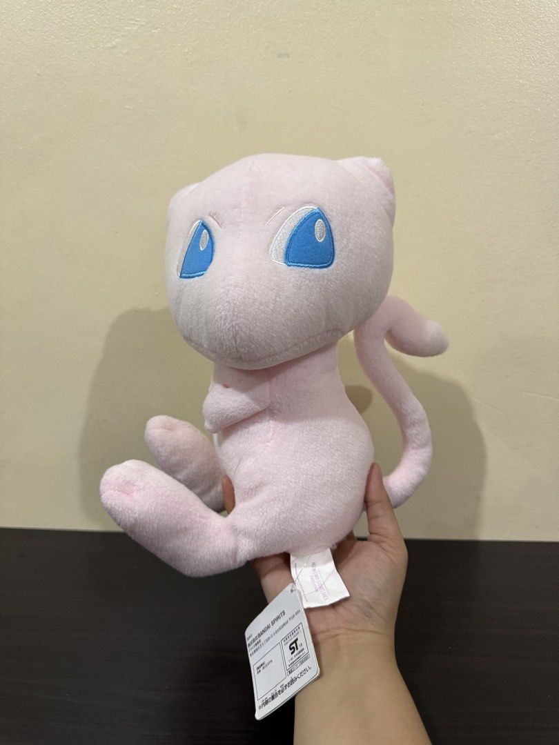 Bandai Spirits Pokémon Mew Plush Toy (Category: Plushies & Soft Toys) located in Cainta. Submitted by mayhroeen (Listing ID 1466966424, Image 2). Description: - Official Banesto prize item by Bandai Spirits (Made in Vietnam) - Features soft pink fabric, cute embroidered blue eyes, and stitched paws - Includes attached paper hang tag and purple tush tag - Built-in white loop string at the top for easy hanging - Condition: Clean and well-maintained