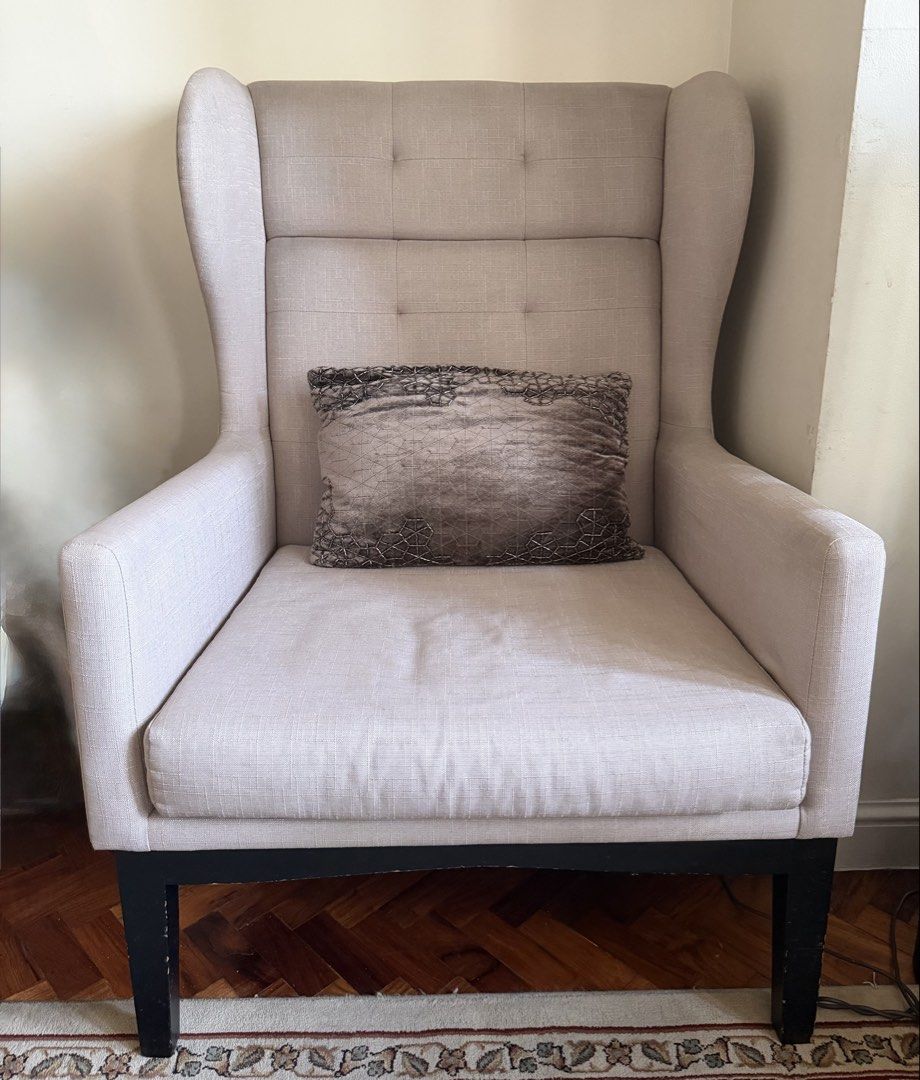Beige Wingback Armchair with Accent Pillow (Category: Chairs) located in Makati City. Submitted by smanisha (Listing ID 1466819473, Image 1). Description: - Elegant beige fabric wingback armchair with classic tufted backrest - Includes a stylish patterned grey accent pillow - Solid black wooden legs (note: minor paint chips and scratches near the bottom, as shown in photos) - Extremely comfortable seating, ideal for a living room or reading corne