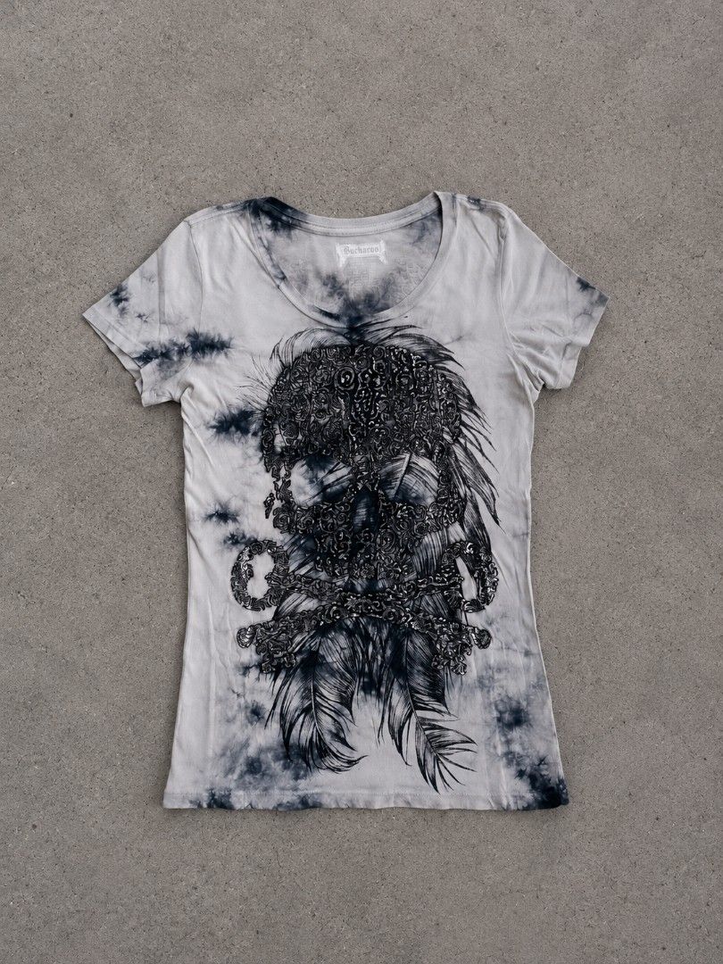 Buckaroo Skull and Feathers Tie-Dye Tee (Category: Blouses) located in Manila. Submitted by thriftnook6111 (Listing ID 1466858370, Image 1). Description: Buckaroo t-shirt in grey with black tie-dye wash. Large intricate skull and feather graphic printed on the front. Back has metallic winged logo detail and cursive branding across the shoulders. Scoop neck and short sleeves. Soft cotton material, comfortable fit. Great casual piece with rock-insp