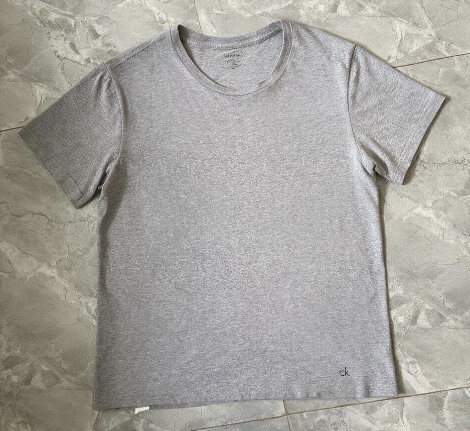 Calvin Klein Grey T-Shirt Size L (Category: Tshirts & Polo Shirts ) located in Iloilo. Submitted by oddforest.c9c7d5 (Listing ID 1466809668, Image 1). Description: - Brand: Calvin Klein - Color: Grey Heather - Size: L - Fit: Regular - Material: Soft cotton - Design: Crew neck with small CK logo near the bottom hem - Condition: Clean and ready to wear.