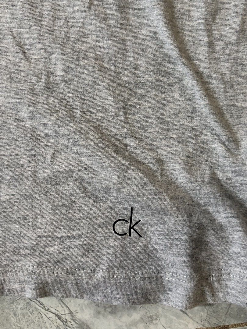 Calvin Klein Grey T-Shirt Size L (Category: Tshirts & Polo Shirts ) located in Iloilo. Submitted by oddforest.c9c7d5 (Listing ID 1466809668, Image 3). Description: - Brand: Calvin Klein - Color: Grey Heather - Size: L - Fit: Regular - Material: Soft cotton - Design: Crew neck with small CK logo near the bottom hem - Condition: Clean and ready to wear.