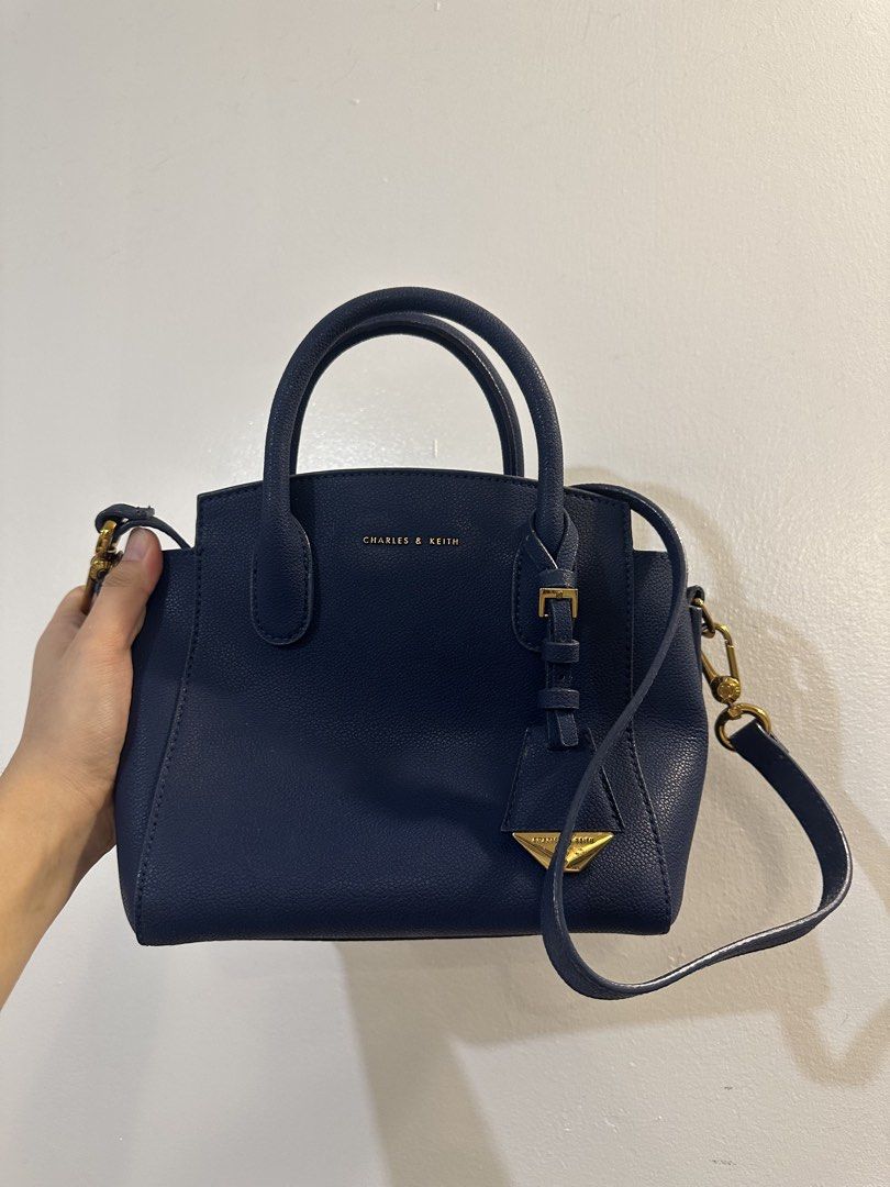 Charles & Keith Navy Blue Handbag with Strap (Category: Luxury Bags & Wallets) located in Makati City. Submitted by cosmicfire.4ba272 (Listing ID 1466929123, Image 1). Description: - Brand: Charles & Keith - Style: Structured handbag with dual top handles and detachable shoulder strap - Color: Classic navy blue with elegant gold hardware accents - Material: Clean pebbled faux leather with secure zipped main compartment - Condition: Good, with a m