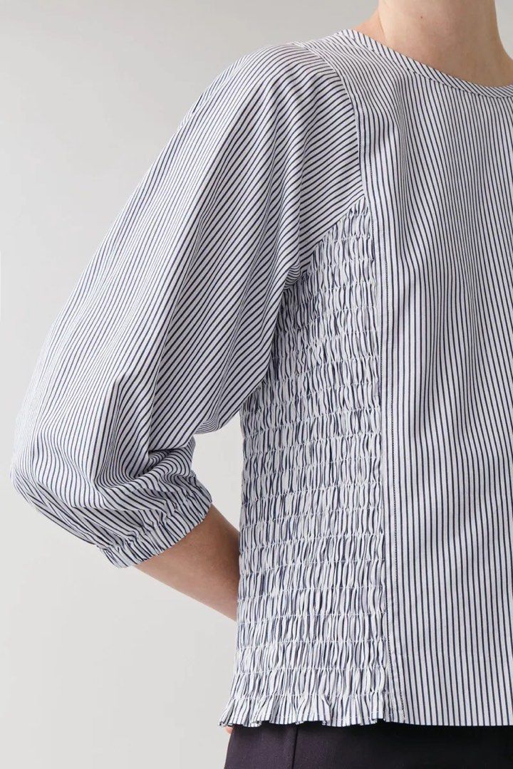 COS Blue and White Striped Smocked Blouse (Category: Blouses) located in Mandaluyong City. Submitted by hopeworldplane (Listing ID 1466924599, Image 3). Description: COS blue and white vertical stripe top. Round neckline with a back zipper closure. Smocked panel details down the sides of the body. Voluminous three-quarter sleeves with elasticated cuffs. Lightweight cotton material. Great minimal piece for everyday outfits or casual office wear. C