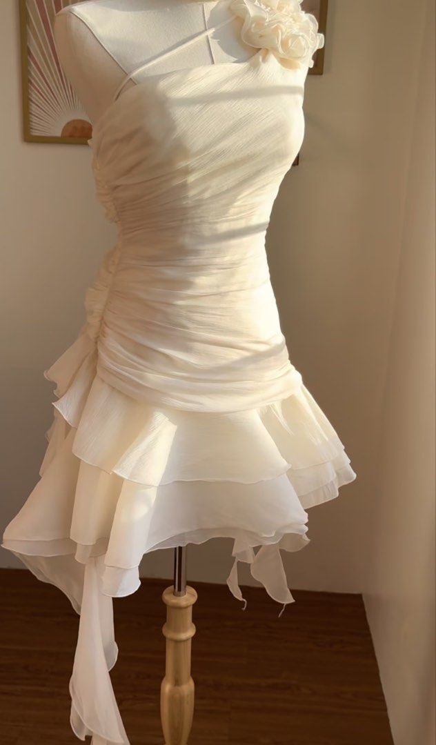 Cream One Shoulder Ruffled Mini Dress (Category: Dresses) located in Pasig City. Submitted by thevintagenook (Listing ID 1466873707, Image 1). Description: - Color: Cream - Style: One-shoulder mini dress with ruched body and asymmetrical draping - Details: Large fabric flower on the strap, layered sheer ruffles with lettuce edges, and a side draped piece - Material: Lightweight chiffon-like fabric with full inner lining - Closure: Invisible side 