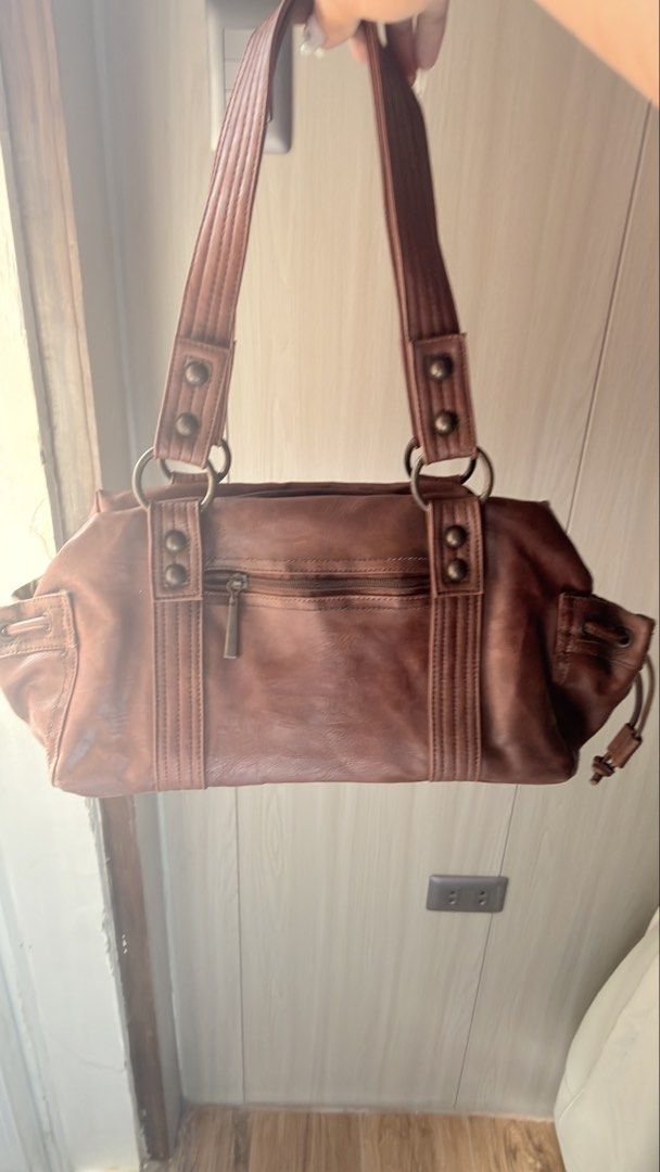 Brown Leather Shoulder bag (Category: Shoulder Bags) located in Manila. Submitted by serraphimav (Listing ID 1466778847, Image 2). Description: - Brand: Crisan - Material: real leather - Color: Brown - Closure: Top zipper closure - Exterior: Front zipper pocket and side drawstring compartments - Straps: Double strap handles with metallic rings and studs - Interior: Beige lining with all-over brand logo and an inner zip pocket.