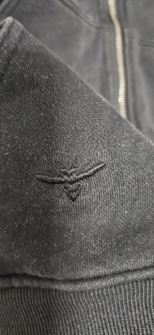 Dior Black Zip-Up Hoodie (Category: Hoodies) located in Santa Maria. Submitted by rommelmateo (Listing ID 1466946623, Image 2). Description: Dior black zip-up hoodie with front pockets. Has a bee embroidery detail on the sleeve and a branded leather tag at the bottom hem with a button closure. Ribbed cuffs and hem. Full zip front with hood. Washed black look with some fading and wear..