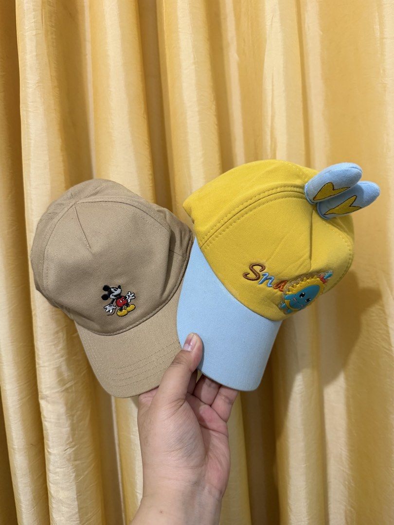 Disney Mickey Mouse and Yellow Sun Kids Caps Bundle (Category: Caps & Hats) located in Binan City. Submitted by prelovedlagunaph (Listing ID 1466968208, Image 1). Description: - Bundle of 2 toddler caps for daily wear - Cap 1: Beige H&M Mickey Mouse embroidered cap, Size 1-2Y with an elastic back strap for an easy fit - Cap 2: Bright yellow and light blue cap featuring a cute cartoon sun and playful ear details - Condition: Clean inside and out, 
