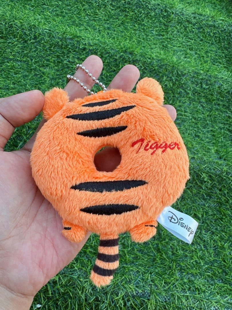 Disney Tigger Donut Plush Keychain Bag Charm (Category: Plushies & Soft Toys) located in Manila. Submitted by ronoarabbit.ph (Listing ID 1466873263, Image 3). Description: - Authentic Disney Tigger plush keychain shaped like a sweet donut - Features bright orange fabric with embroidered black tiger stripes and Tigger's signature - Detailed with cute little ears, a striped tail, and a secure ball chain - Official Disney tag attached; Made in China