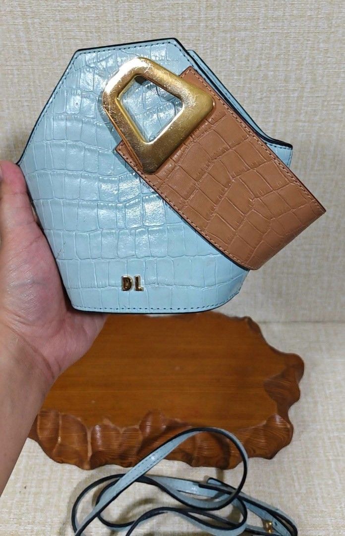 DL Two-Tone Crocodile Textured Bucket Bag with Strap (Category: Luxury Bags & Wallets) located in Manila. Submitted by boldfire_315559 (Listing ID 1466808970, Image 2). Description: - Style: Light blue and tan crocodile embossed bucket bag - Design: Unique trapezoid shape with structured top handle and geometric gold-tone buckle - Branding: Gold DL logo lettering on the front base - Versatility: Includes a matching detachable long shoulder strap 