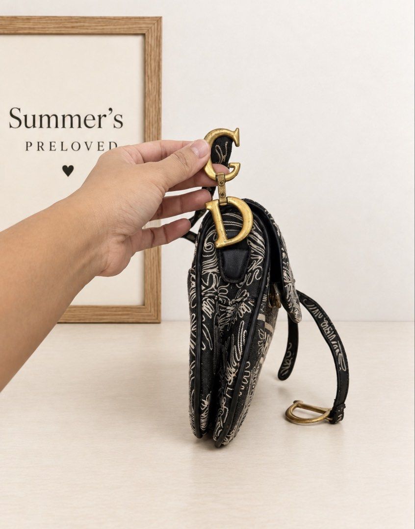 Dyorgina saddle bag (Category: Tote Bags) located in Taguig. Submitted by summers.preloved (Listing ID 1466848319, Image 3). Description: 👜 BAG DETAILS 🖤 Color: Black with cream ornamental motifs and black trim. 🧵 Exterior: Canvas with intricate scroll-and-leaf detailing and a prominent “DYORGINA PARIS” band across the front. ✨ Silhouette: Asymmetric saddle shape with a curved base and shaped flap. 🤎 Trim: Smooth black edging, piping, and str