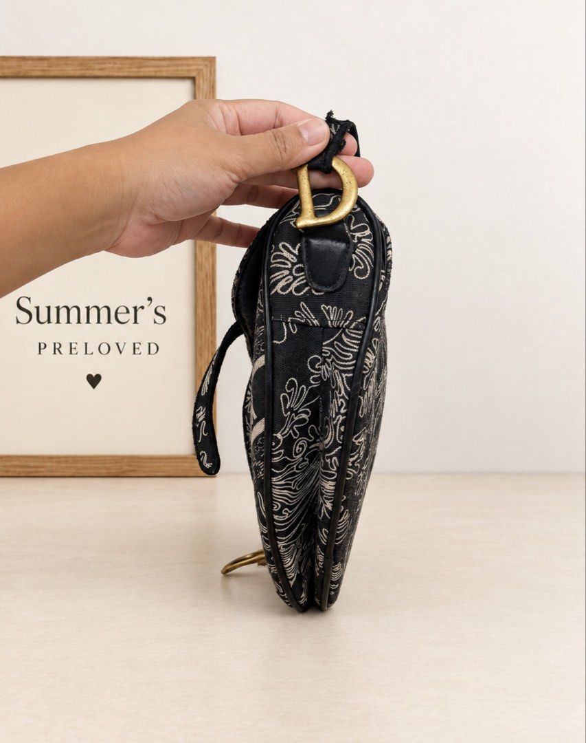 Dyorgina saddle bag (Category: Tote Bags) located in Taguig. Submitted by summers.preloved (Listing ID 1466848319, Image 2). Description: 👜 BAG DETAILS 🖤 Color: Black with cream ornamental motifs and black trim. 🧵 Exterior: Canvas with intricate scroll-and-leaf detailing and a prominent “DYORGINA PARIS” band across the front. ✨ Silhouette: Asymmetric saddle shape with a curved base and shaped flap. 🤎 Trim: Smooth black edging, piping, and str