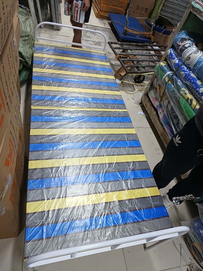 Foldable Single Bed with Striped Mattress (Category: Bed Frames & Mattresses) located in Caloocan City. Submitted by swiftflower_802790 (Listing ID 1466948105, Image 1). Description: - Foldable single bed with sturdy white metal frame - Comfortable mattress with blue, yellow, and grey stripes - Folds in half easily for compact storage and moving - Great space saver ideal for small rooms or unexpected guests.
