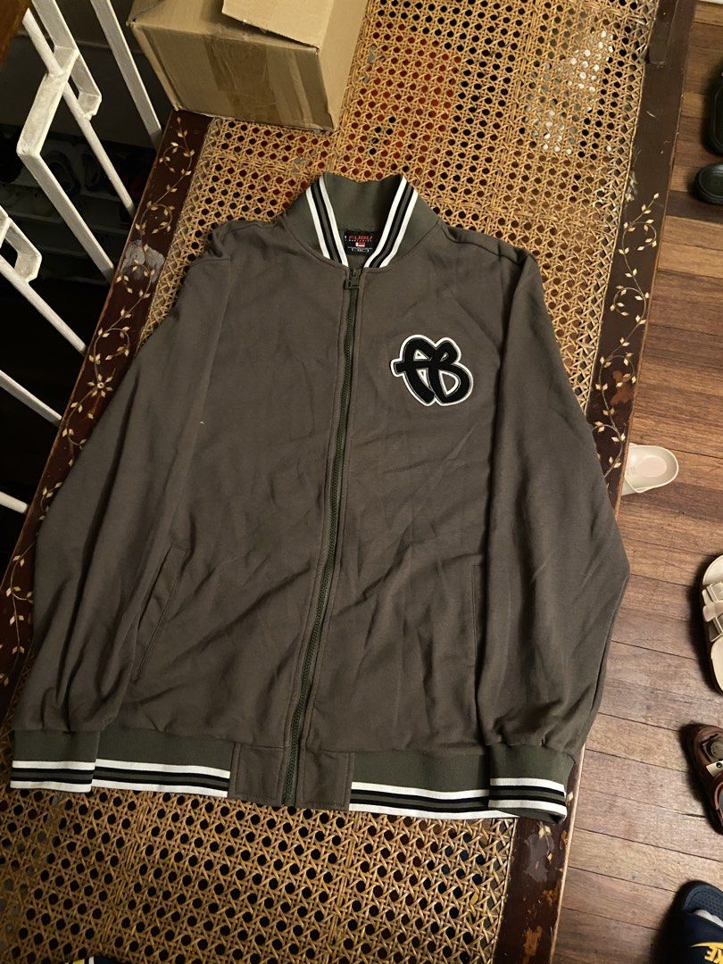 FUBU Olive Green Bomber Jacket with Varsity Stripes (Category: Coats, Jackets and Outerwear) located in San Miguel. Submitted by cashcarti222 (Listing ID 1466916022, Image 1). Description: - Brand: FUBU - Color: Olive green - Design: Full-zip jacket with black and white varsity stripes on the collar, cuffs, and hem - Branding: Small FUBU monogram patch on the left chest and large cursive FUBU lettering patch across the back - Details: Ribbed knit