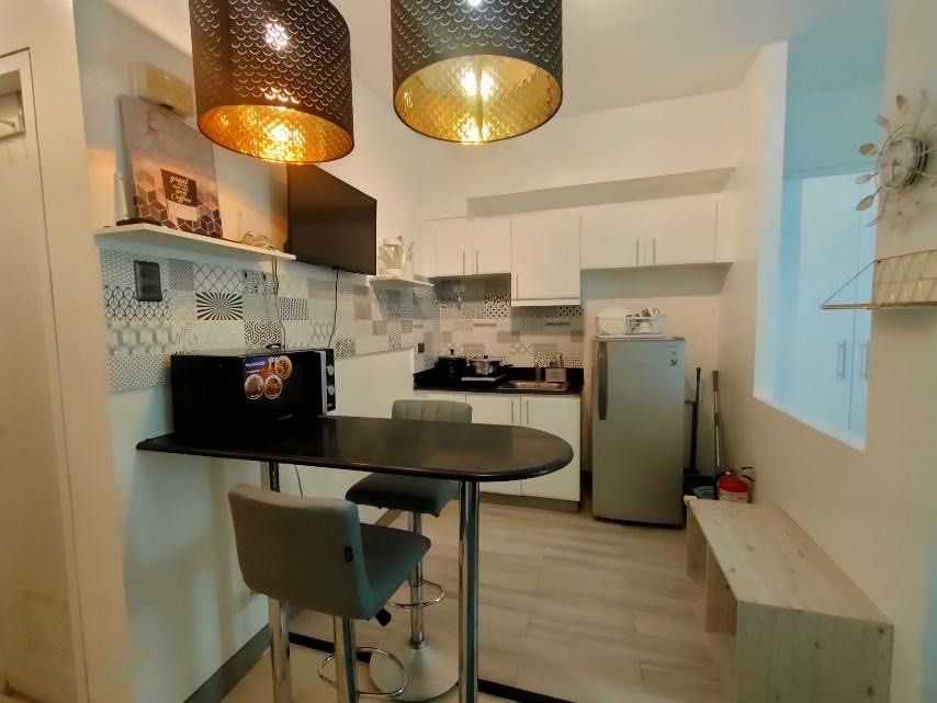 Fully furnished studio apartment interior setup with bed and dining (Category: Apartments & Condos) located in Makati City. Submitted by theacd (Listing ID 1466907671, Image 1). Description: - Complete studio apartment interior setup, ready for move-in - Double bed with stylish blue bedding and fluffy teal rug - Dining counter paired with two grey bar stools - Fully equipped kitchen area with overhead cabinets, refrigerator, and microwave - Elega