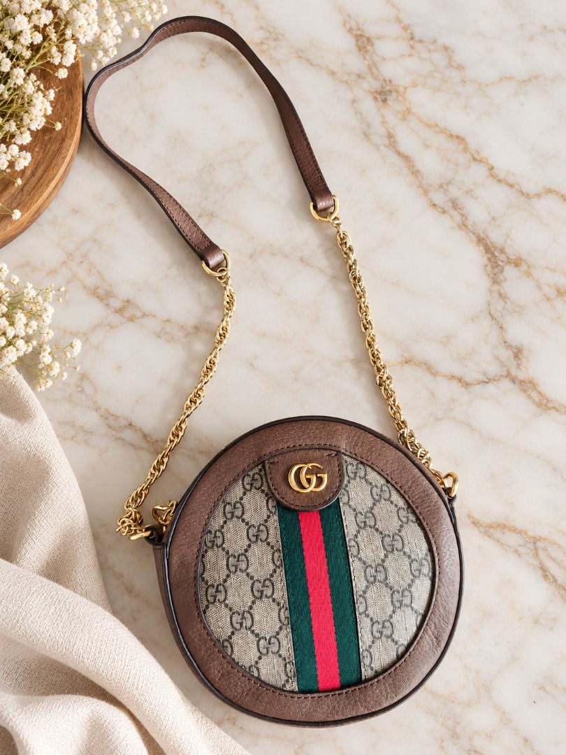 GG Small Round Sling Bag (Category: Luxury Bags & Wallets) located in Basud. Submitted by ClaireLavin (Listing ID 1466785965, Image 1). Description: 🤎 Chic Round Chain Bag – Classic Brown Elevate your everyday style with this round bag featuring a beige monogram-print body, brown leather-look trim, a green and red center stripe, and a gold-tone interlocking logo accent. Complete with a gold-tone chain strap and zipper closure, it’s a stylish acc