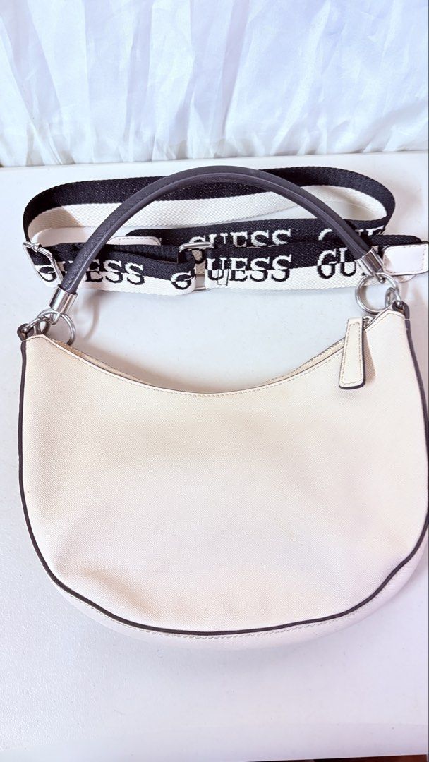 Guess Cream Shoulder Bag with Interchangeable Straps (Category: Shoulder Bags) located in Pateros City. Submitted by marifernandez (Listing ID 1466783771, Image 2). Description: Original preloved Guess cream-colored hobo bag with structured design. Silver hardware and black trim details. Top zipper closure opens to branded lining with internal pockets. Includes both a short dark top handle and a thick, branded canvas crossbody strap. Clean interi