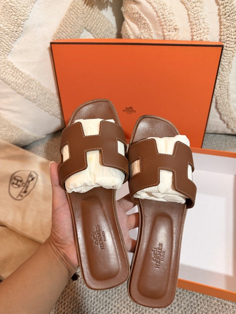 Hermes Oran Sandals Brown (Category: Flats & Sandals) located in San Pedro. Submitted by kathlynaviles_ (Listing ID 1466946314, Image 3). Description: - Authentic Hermes Oran Sandals in a rich brown leather colorway - Features the iconic cutout H strap design with a comfortable flat slide style - Stamped Hermès Paris on the footbed for guaranteed authenticity - Comes with complete inclusions: original orange box and dust bags - Perfect luxury eve
