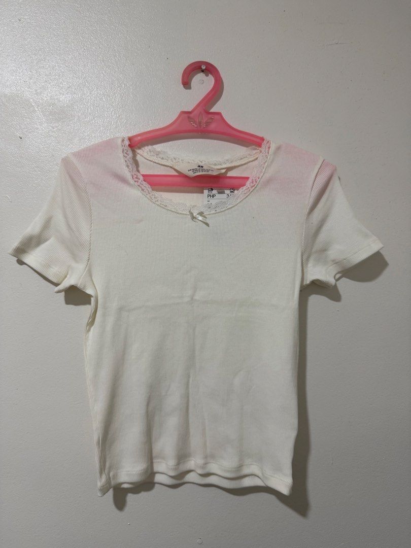 H&M White Ribbed Lace Trim Top (Category: Shirts) located in Manila. Submitted by itsmerawrs (Listing ID 1466789318, Image 1). Description: - Brand: H&M (Tag still attached) - Color: Clean white - Material: Soft and stretchy ribbed fabric - Fit: Fitted cut with short sleeves - Details: Scalloped lace trim on round neckline with a tiny center bow accent - Condition: Brand new, no stains or flaws.