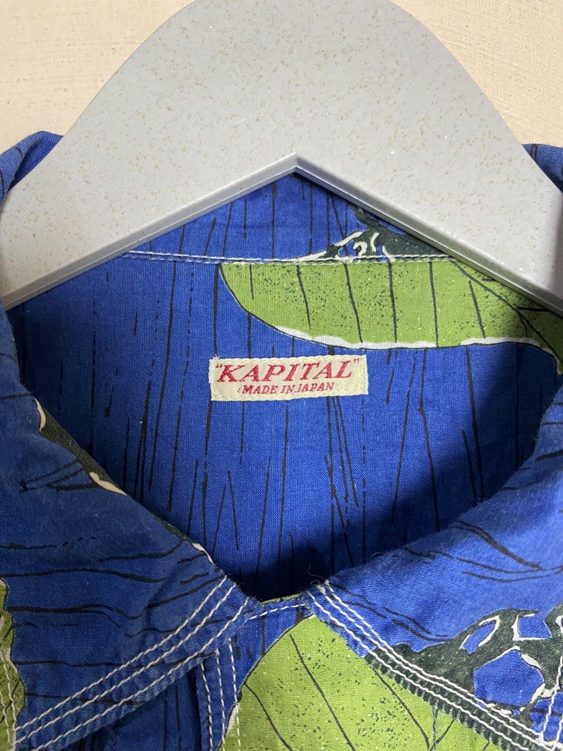 KAPITAL Leaf Print Indigo Aloha Shirt (Category: Luxury Apparel) located in Naga. Submitted by dailyshipped (Listing ID 1466801992, Image 3). Description: It features Kapital’s signature indigo-dyed cotton base with a distinctive, graphic all-over print of green leaves designed with realistic “insect-bitten” detailing (mushikui). Key technical signatures of this garment include triple-stitch contrast needlework on the collar, four-track structura