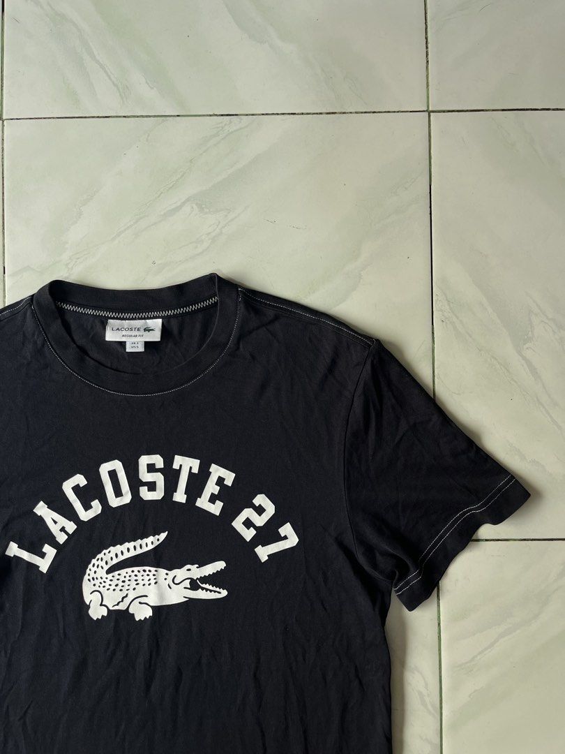 Lacoste 27 Black T-Shirt Regular Fit (Category: Tshirts & Polo Shirts ) located in Naga. Submitted by stoob.finds (Listing ID 1466800041, Image 1). Description: - Brand: Lacoste - Color: Black with white graphic and contrast stitching - Size: US Small (FR 3) - Fit: Regular fit - Design: Large 'Lacoste 27' chest print with classic crocodile logo and white accent stitching - Condition: Clean and ready to wear -Length 25 -width 18.5.
