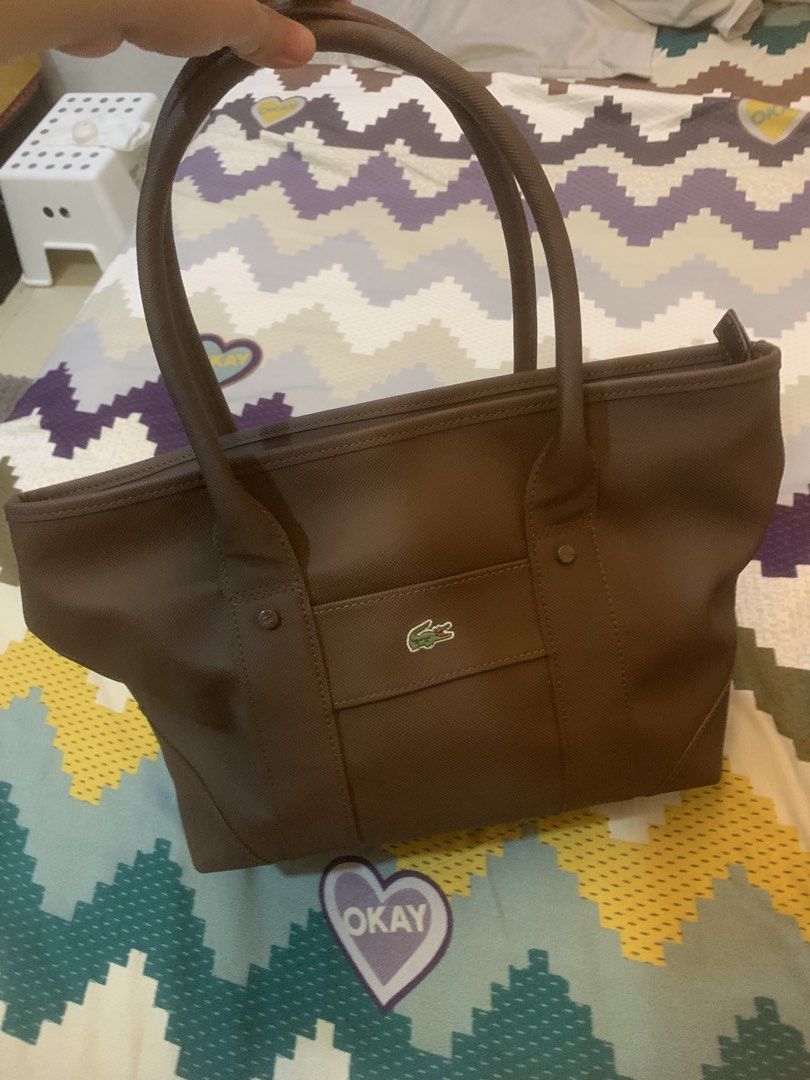 Lacoste Brown Small Shopping Bag (Category: Tote Bags) located in Cainta. Submitted by JCJ_shoppe (Listing ID 1466847711, Image 1). Description: Brown Lacoste small shopping bag with structured handles and front pocket. Iconic crocodile logo patch stitched right on the front. Top zipper closure to keep items secure. Inside features a white and black grid pattern lining with an extra zippered pocket and embossed Lacoste leather tag. Clean canvas e
