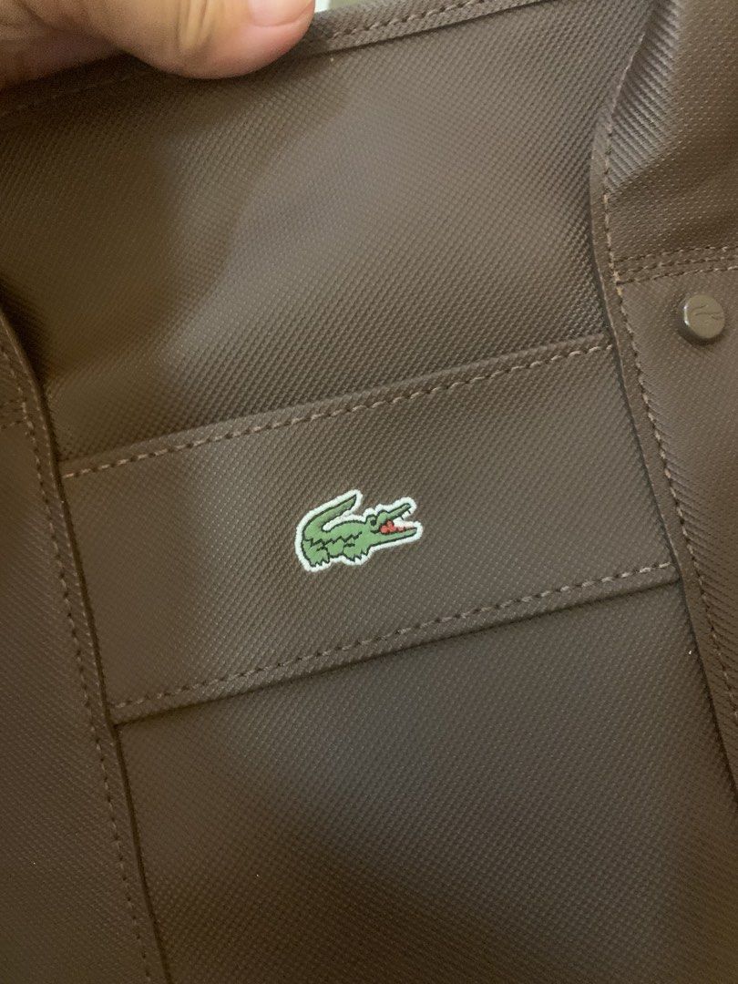 Lacoste Brown Small Shopping Bag (Category: Tote Bags) located in Cainta. Submitted by JCJ_shoppe (Listing ID 1466847711, Image 3). Description: Brown Lacoste small shopping bag with structured handles and front pocket. Iconic crocodile logo patch stitched right on the front. Top zipper closure to keep items secure. Inside features a white and black grid pattern lining with an extra zippered pocket and embossed Lacoste leather tag. Clean canvas e