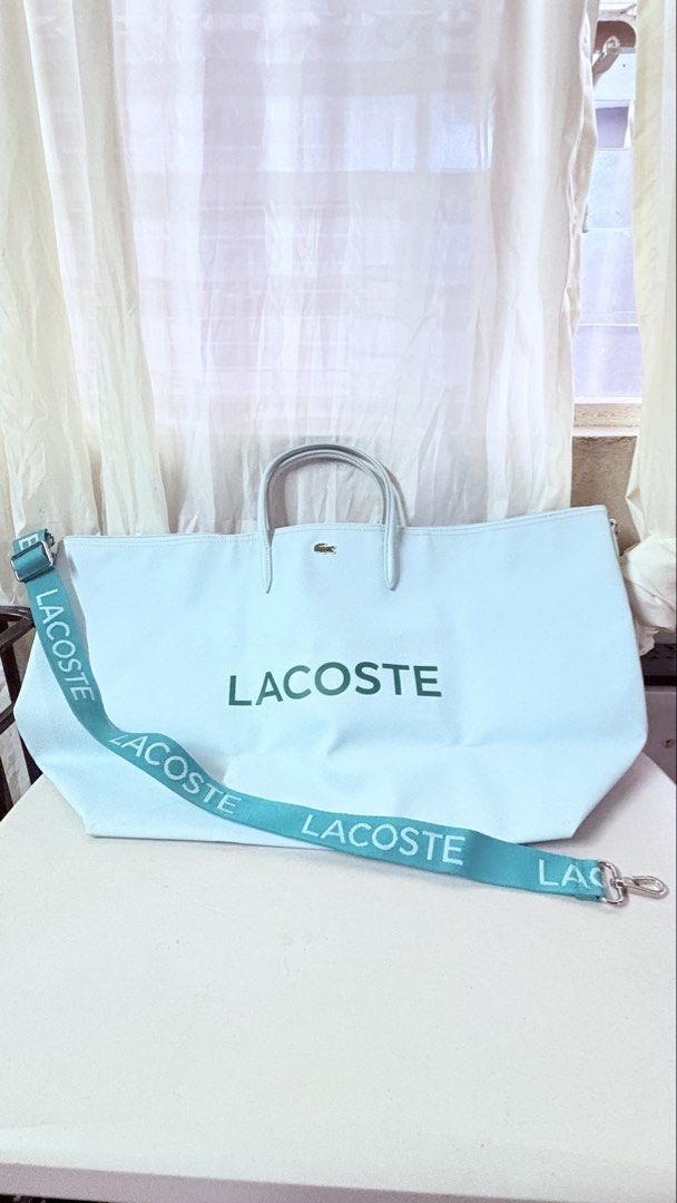 Lacoste Light Blue Canvas Tote Bag With Strap (Category: Tote Bags) located in Pateros City. Submitted by marifernandez (Listing ID 1466784261, Image 1). Description: - Preloved Authentic Lacoste canvas travelling tote bag in light blue - Features the iconic green Lacoste logo on the front and a metal crocodile badge near the top handles - Includes a matching turquoise shoulder strap with repeating Lacoste lettering - Interior comes with a practi