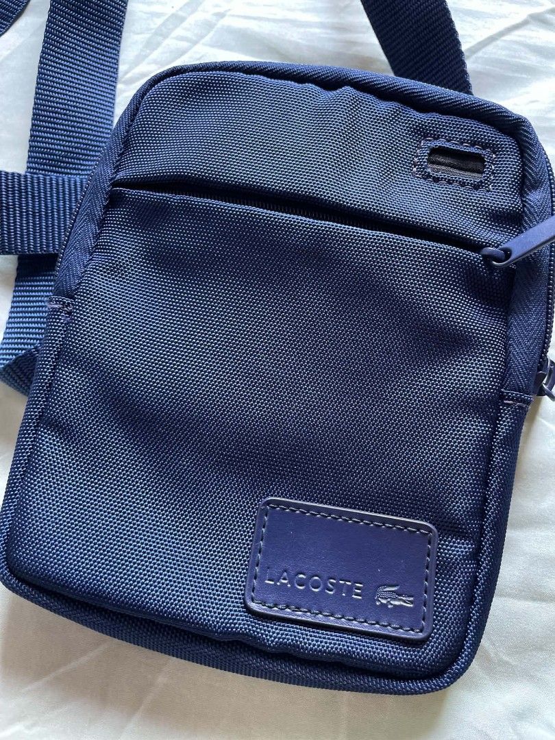 Lacoste Navy Blue Crossbody Bag (Category: Cross-body Bags) located in Manila. Submitted by xtinamendo00659 (Listing ID 1466836448, Image 3). Description: - Authentic navy blue Lacoste crossbody bag made from durable nylon - Adjustable shoulder strap for a comfortable, custom fit - Secure main compartment and front zip pocket with branded zipper pulls - Features the classic rectangular Lacoste logo patch on the front - Impeccably clean interior a