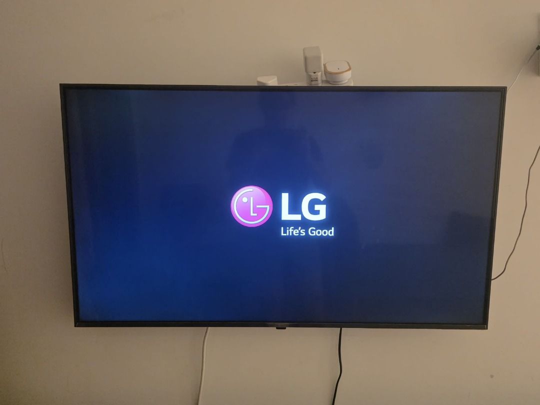 LG Smart TV （分類：電視）位於 Hong Kong。 由 amitdias0928157 提交（商品編號 1466953436，圖片 2）。簡介： LG flat screen television mounted on a wall. Clear display showing startup logo and video playback. Standard thin black bezel design with visible plug adapters sitting on top frame. Wall mount setup with power cords hanging below. Tested and working normally.。