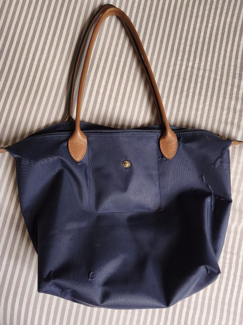 Longchamp Navy Blue Tote Bag (Category: Tote Bags) located in Paranaque City. Submitted by airico (Listing ID 1466778427, Image 1). Description: - Brand: Original Longchamp - Style: Nylon Tote Bag - Color: Deep navy blue with brown leather handles and flap - Hardware: Gold-tone - Closure: Zip top with snap flap with issue - Interior: Clean with convenient slip pockets - Condition: Pre-loved with signs of regular daily use; minor dark stain near t