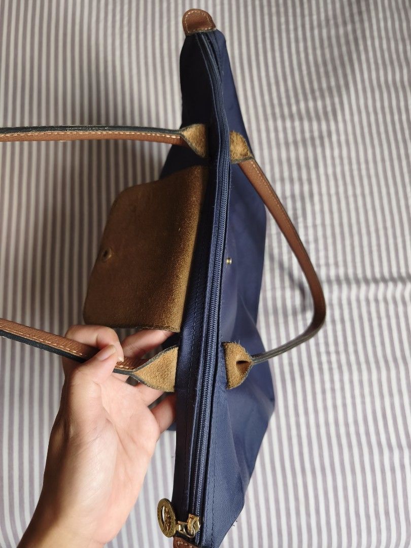 Longchamp Navy Blue Tote Bag (Category: Tote Bags) located in Paranaque City. Submitted by airico (Listing ID 1466778427, Image 2). Description: - Brand: Original Longchamp - Style: Nylon Tote Bag - Color: Deep navy blue with brown leather handles and flap - Hardware: Gold-tone - Closure: Zip top with snap flap with issue - Interior: Clean with convenient slip pockets - Condition: Pre-loved with signs of regular daily use; minor dark stain near t