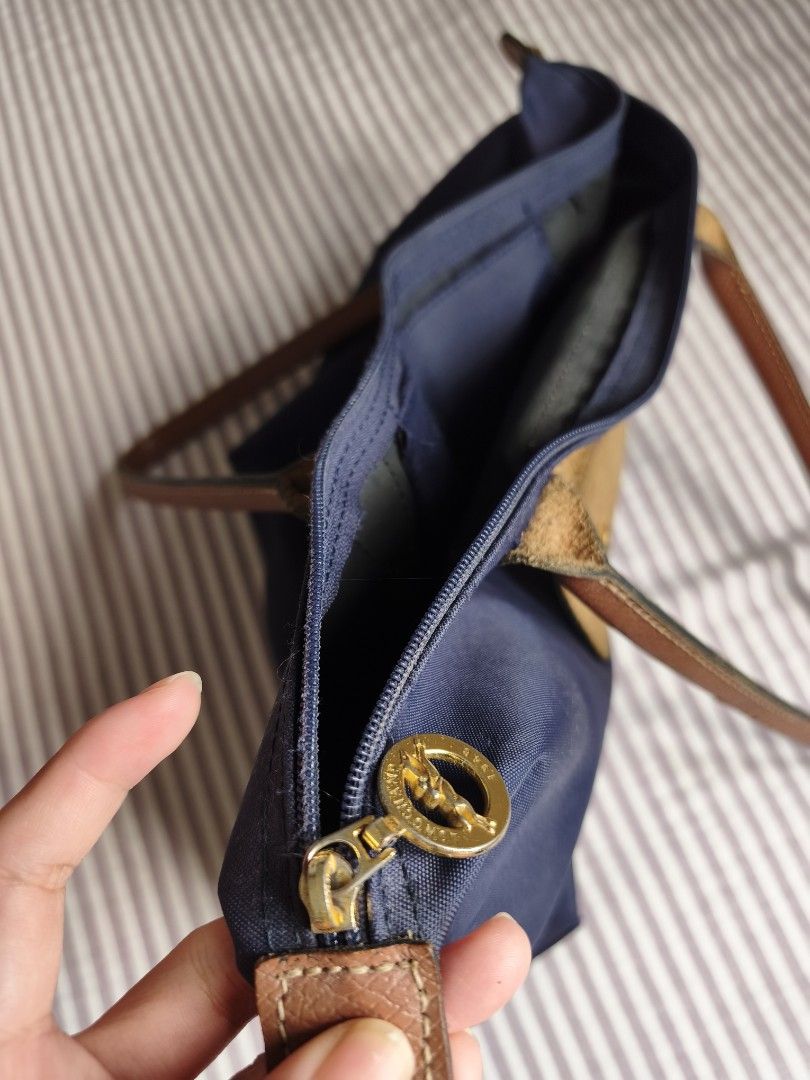 Longchamp Navy Blue Tote Bag (Category: Tote Bags) located in Paranaque City. Submitted by airico (Listing ID 1466778427, Image 3). Description: - Brand: Original Longchamp - Style: Nylon Tote Bag - Color: Deep navy blue with brown leather handles and flap - Hardware: Gold-tone - Closure: Zip top with snap flap with issue - Interior: Clean with convenient slip pockets - Condition: Pre-loved with signs of regular daily use; minor dark stain near t