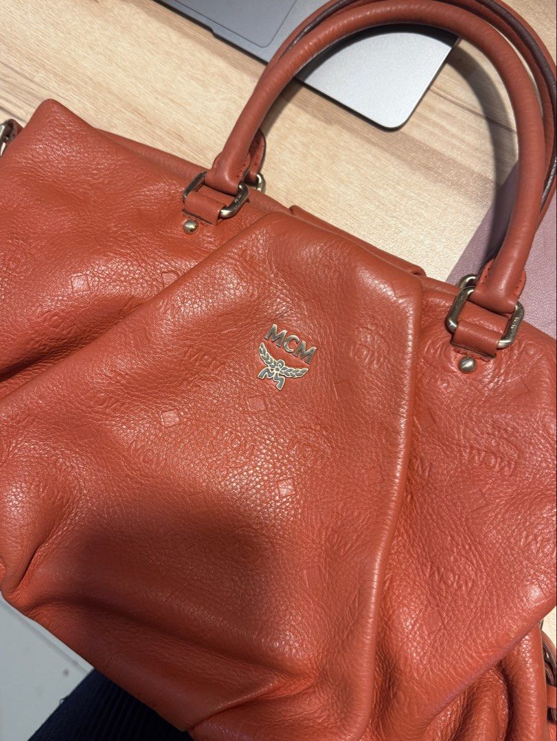 MCM Orange Leather Tote Shoulder Bag (Category: Luxury Bags & Wallets) located in Cebu City. Submitted by declutterbarbie_ (Listing ID 1466822025, Image 2). Description: Orange textured leather handbag from MCM. Stamped monogram pattern all over. Dual top handles plus a detachable shoulder strap. Gold tone hardware and logo plaque on front. Bright orange fabric interior lining includes zip pockets and slip compartments. Roomy everyday tote design