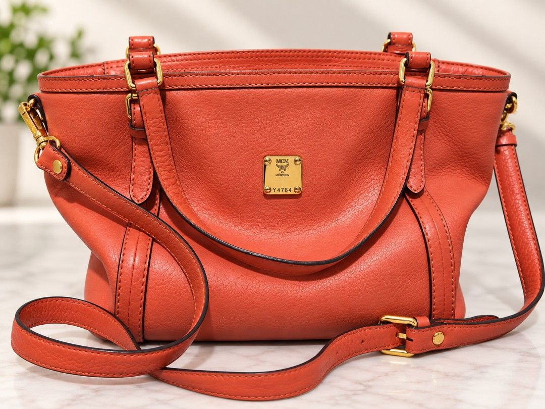 MCM Orange Leather Tote Shoulder Bag (Category: Cross-body Bags) located in Manila. Submitted by coolbear.5772e6 (Listing ID 1466859123, Image 1). Description: - Brand: MCM - Material: Premium pebble leather in bright coral orange - Hardware: Gold-tone with front logo plaque and serial number Y4784 - Straps: Dual top handles + adjustable, detachable shoulder strap - Base: Structured bottom with 5 protective metal feet - Condition/Interior: Clean 