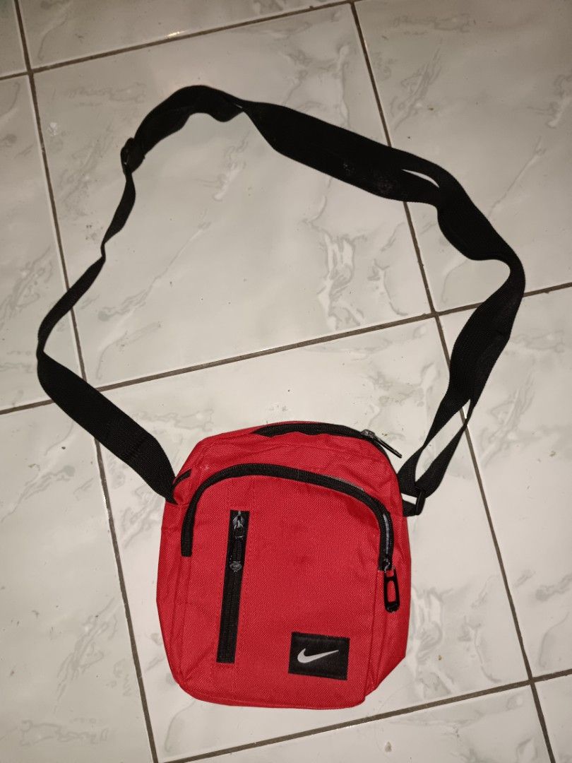 Nike Red Crossbody Bag (Category: Sling Bags) located in Manila. Submitted by caaths_collection (Listing ID 1466960294, Image 1). Description: pls read - as is - sira po yung zipper niya dipo malock - Color: Bright red with black adjustable strap - Storage: Front pocket with zipper closure and vertical zip compartment - Material: Durable canvas-like fabric - Condition: Minimal wear, great for carrying daily essentials hands-free.