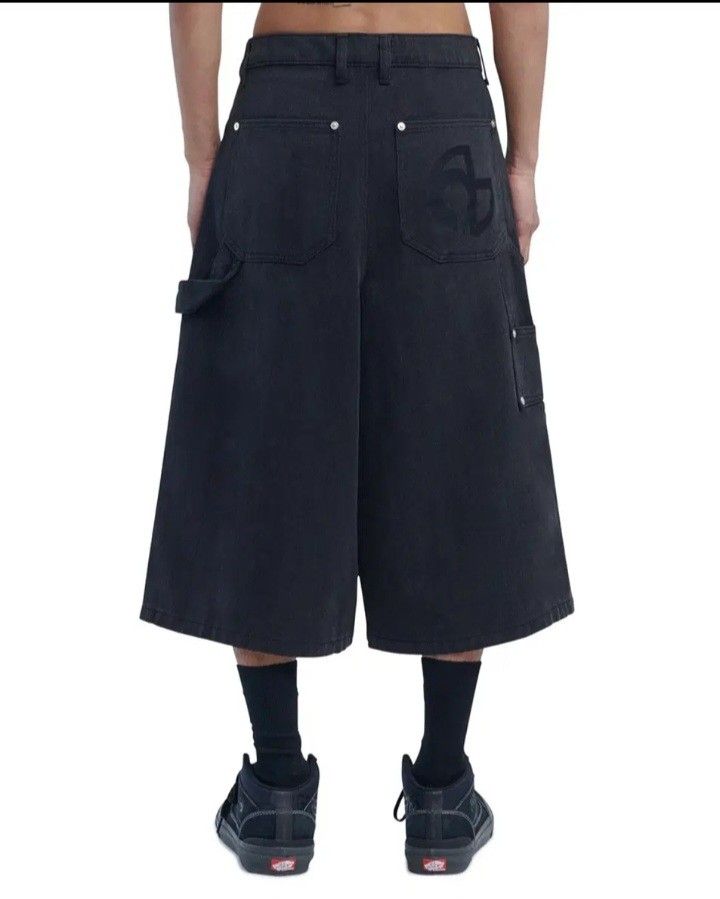 Nomanual Black Denim Carpenter Double Kner Not Stretch (Category: Shorts) located in Valenzuela. Submitted by AnahThrift (Listing ID 1466869300, Image 2). Description: - Brand: Nomanual - Item: Denim Jorts / Shorts - Color: Black - Size: Medium - Fit: Wide-leg, knee-length - Details: Carpenter style pockets, silver-tone hardware studs, embroidered logo on back pocket - Fabric: Thick, structured black denim - Style: Streetwear, easy to pair with t