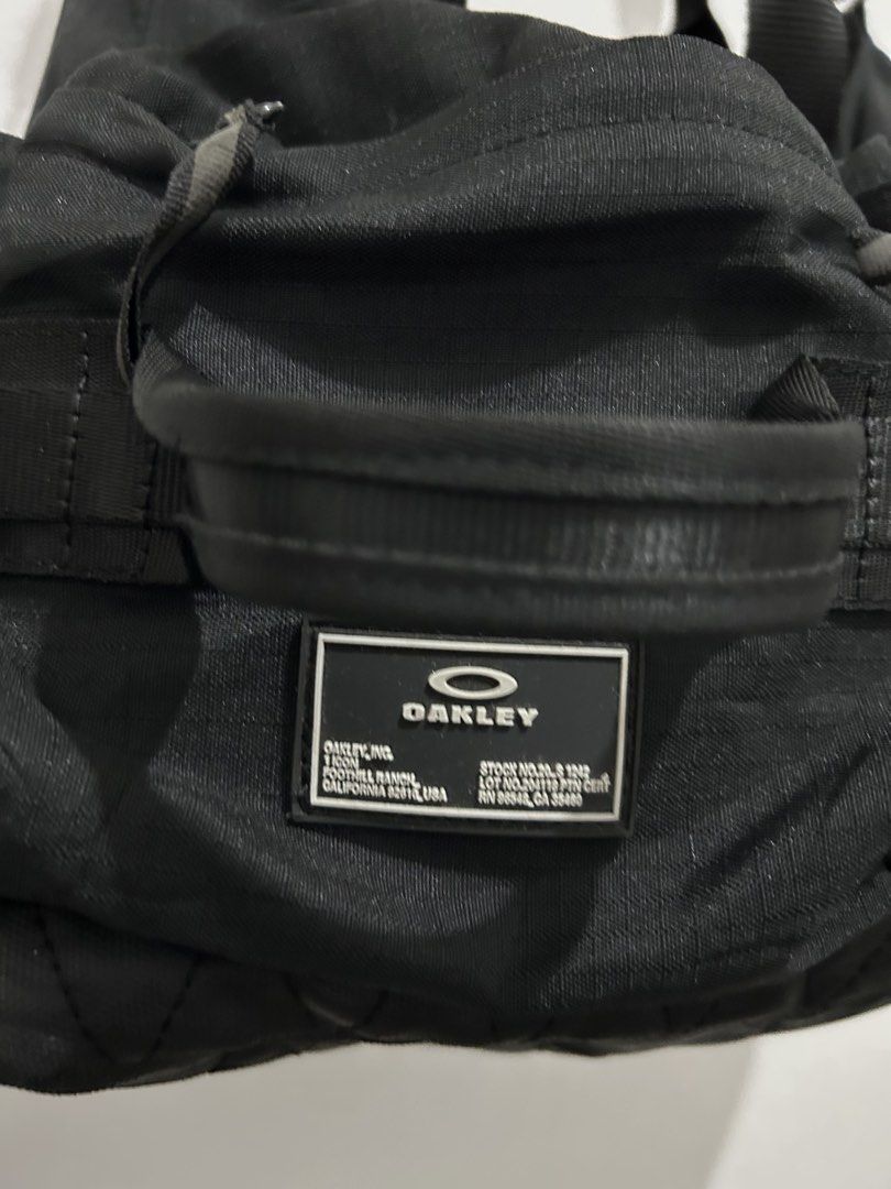 Oakley Black Utility Shoulder Bag Tote (Category: Shoulder Bags) located in Angeles City. Submitted by cassey_phoenix (Listing ID 1466885774, Image 3). Description: - Brand: Oakley - Type: Utility shoulder bag and tote - Material: Heavy-duty black nylon with a quilted bottom panel - Branding: Big white Oakley logo on front and rubberized patch with stock number details - Storage: Multiple zippered exterior pockets and side compartments with draws