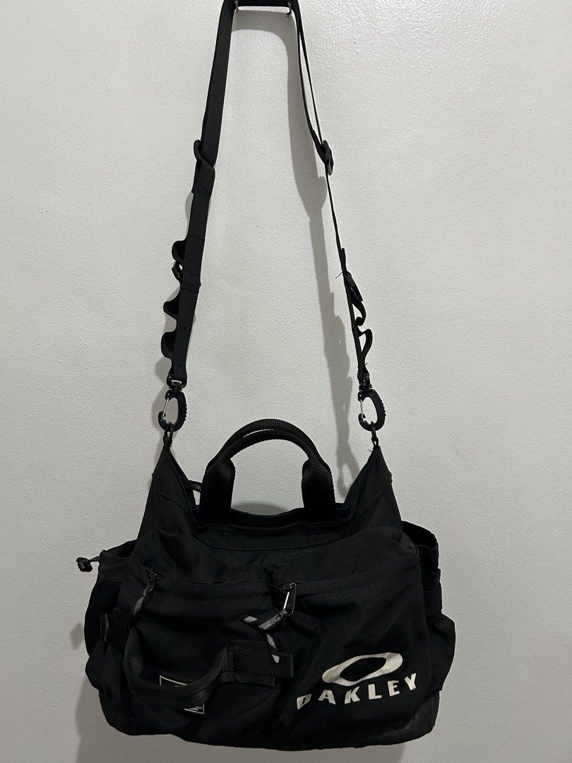 Oakley Black Utility Shoulder Bag Tote (Category: Shoulder Bags) located in Angeles City. Submitted by cassey_phoenix (Listing ID 1466885774, Image 2). Description: - Brand: Oakley - Type: Utility shoulder bag and tote - Material: Heavy-duty black nylon with a quilted bottom panel - Branding: Big white Oakley logo on front and rubberized patch with stock number details - Storage: Multiple zippered exterior pockets and side compartments with draws