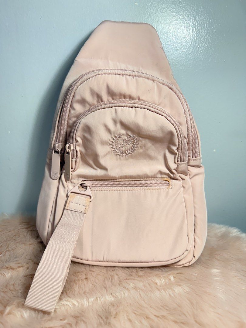 Pink Nylon Sling Bag Crossbody Backpack (Category: Cross-body Bags) located in Quezon City. Submitted by shaberbree (Listing ID 1466908246, Image 1). Description: - Color: Soft pink - Material: Durable nylon - Design: Multiple zippered compartments with an embroidered circular logo - Strap: Adjustable thick shoulder strap with side-release buckle - Interior: Clean lining with an extra zipper pocket - Style: Handy everyday crossbody bag for hands-