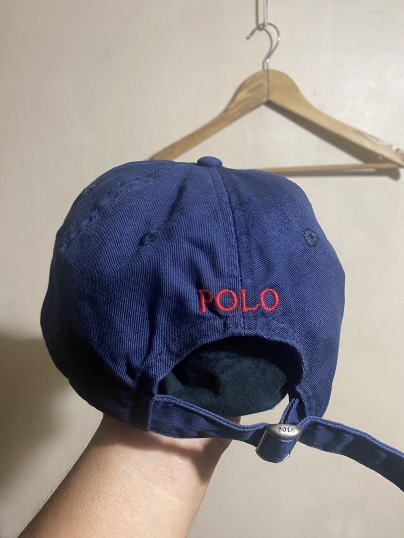 Polo Ralph Lauren Navy Blue Cap (Category: Caps & Hats) located in Bocaue. Submitted by pards23 (Listing ID 1466903768, Image 3). Description: - Brand: Polo Ralph Lauren - Color: Classic navy blue with red accents - Design: Red embroidered pony logo on the front and 'POLO' embroidery above the back strap - Material: Sturdy, structured cotton fabric - Fit: Fully adjustable strap with an embossed metal buckle - Condition: Clean and well-maintained 