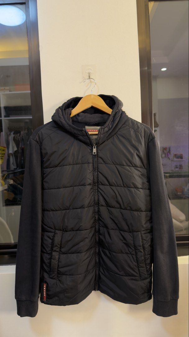 Prada Black Puffer Hoodie Jacket Size XL (Category: Coats, Jackets and Outerwear) located in Paranaque City. Submitted by mykapoynton (Listing ID 1466959937, Image 2). Description: Prada Black Puffer Hoodie Jacket Size XL - Color: Black - Size: XL - Material: Quilted front panel with cotton jersey sleeves and back - Features: Full zip closure, attached hood, and front pockets - Details: Iconic red Prada logo tag on lower hem and inner collar - Co