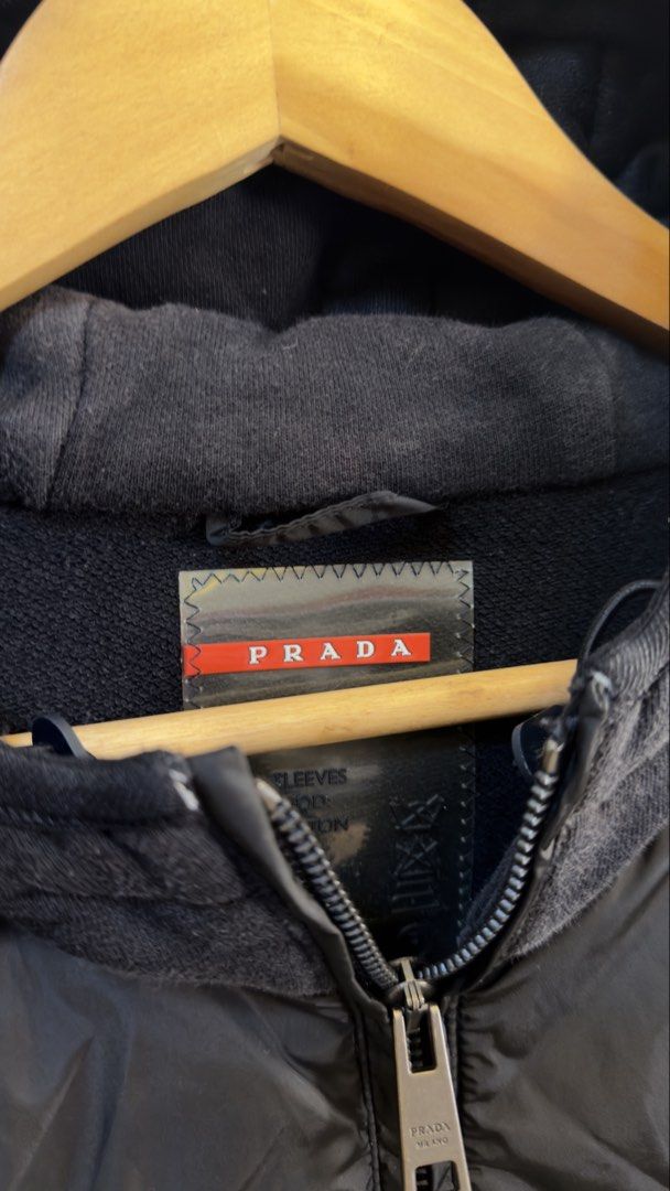 Prada Black Puffer Hoodie Jacket Size XL (Category: Coats, Jackets and Outerwear) located in Paranaque City. Submitted by mykapoynton (Listing ID 1466959937, Image 3). Description: Prada Black Puffer Hoodie Jacket Size XL - Color: Black - Size: XL - Material: Quilted front panel with cotton jersey sleeves and back - Features: Full zip closure, attached hood, and front pockets - Details: Iconic red Prada logo tag on lower hem and inner collar - Co