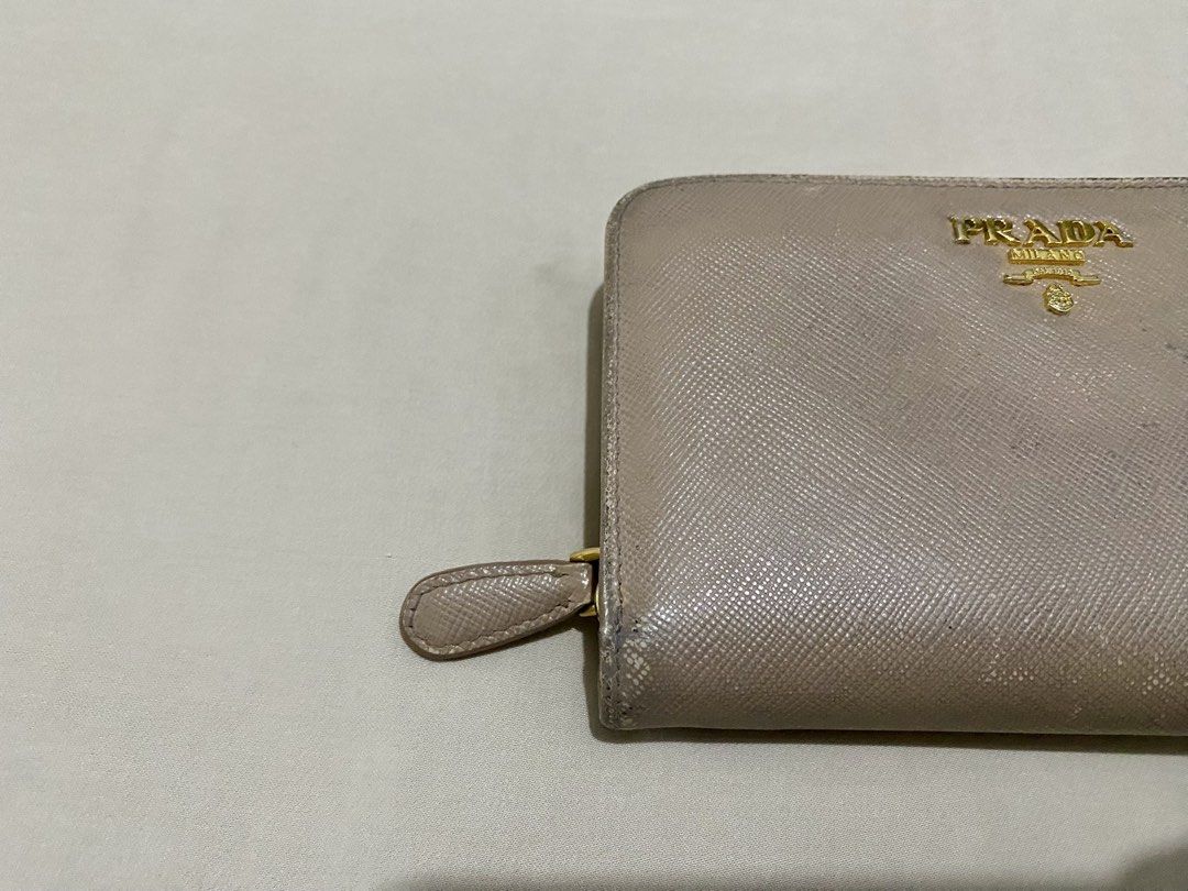 Prada Saffiano Leather Bi-fold Wallet Beige (Category: Wallets & Card holders) located in Makati City. Submitted by purple101395 (Listing ID 1466884170, Image 2). Description: Signs of wear around the edges, corners, and flap closure. Button and zipper works well. No inclusions..