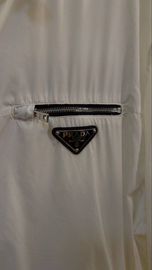 Prada White Hooded Windbreaker Jacket Size 56 (Category: Coats, Jackets and Outerwear) located in Paranaque City. Submitted by mykapoynton (Listing ID 1466960127, Image 3). Description: Prada White Hooded Windbreaker Jacket - Item: Hooded Windbreaker - Color: Clean White - Size: 56 (Tag inside) - Features: Full front zip, adjustable drawstrings at the hood - Pockets: Zippered chest pocket with metal logo plaque and two side zip pockets - Details: