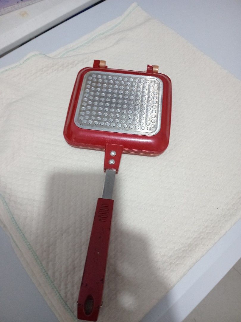 Red Double-Sided Sandwich Maker Pan (Category: Cookware & Accessories) located in Marikina City. Submitted by joyful.finds (Listing ID 1466970533, Image 1). Description: - Vibrant red double-sided sandwich maker for delicious stove-toasted sandwiches - Textured exterior base ensures even heat distribution - Long handle with a comfortable red grip and hanging hole for easy storage - Secure metal hinges connect both pan halves safely - Compact squa