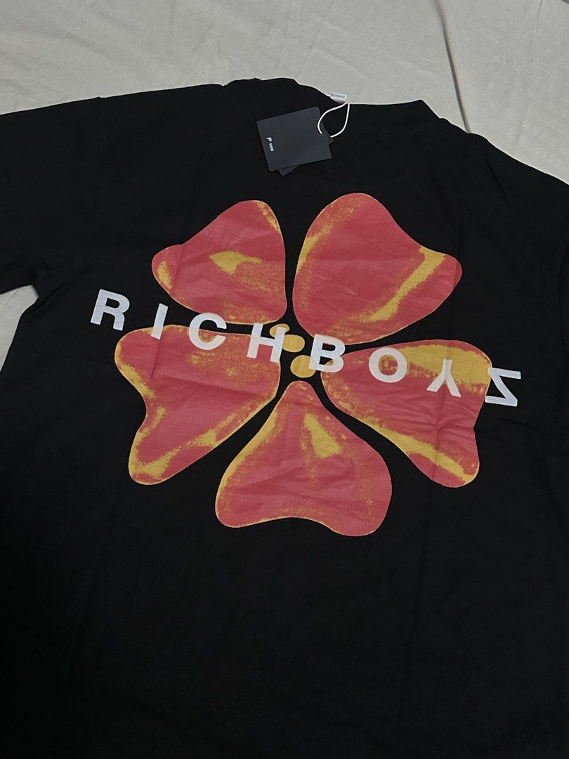 Richboyz shirt (Category: Shirts) located in Manila. Submitted by jmdrgooddeals (Listing ID 1466911971, Image 3). Description: - Brand: Richboyz - Color: Black - Size: Medium (M) - Condition: Brand new with original store tags attached - Design: Small white logo on front chest; large red and yellow flower graphic with white branding on the back - Fit/Style: Crew neck, short sleeves.