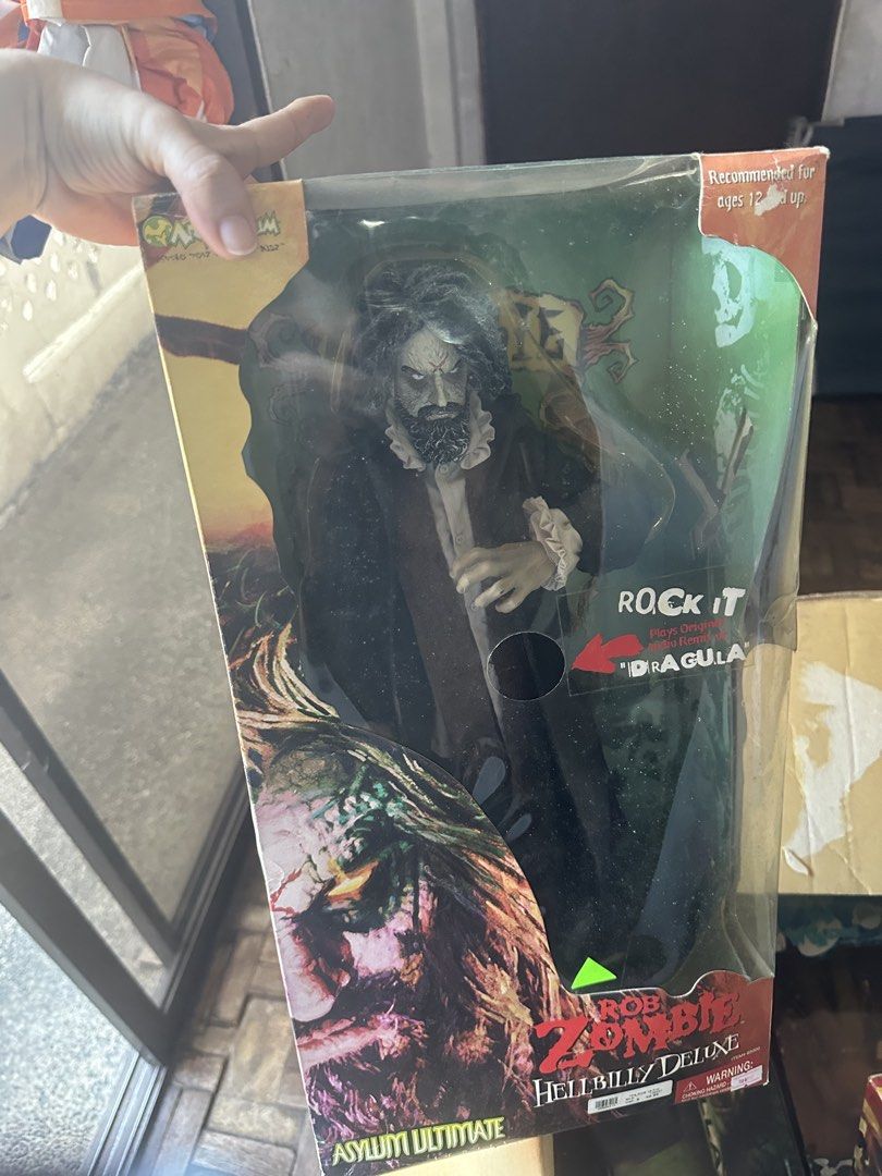 Rob Zombie Hellbilly Deluxe Asylum Ultimate Action Figure (Category: Figurines & Statues) located in Quezon City. Submitted by lylesofia (Listing ID 1466961682, Image 1). Description: - Item: Rob Zombie Hellbilly Deluxe Asylum Ultimate Action Figure - Condition: Box shows minor shelf wear and scuffs on the plastic window from storage; figure inside is carefully stored - Special Feature: Plays the original audio remix of Dragula - Perfect for: Fan
