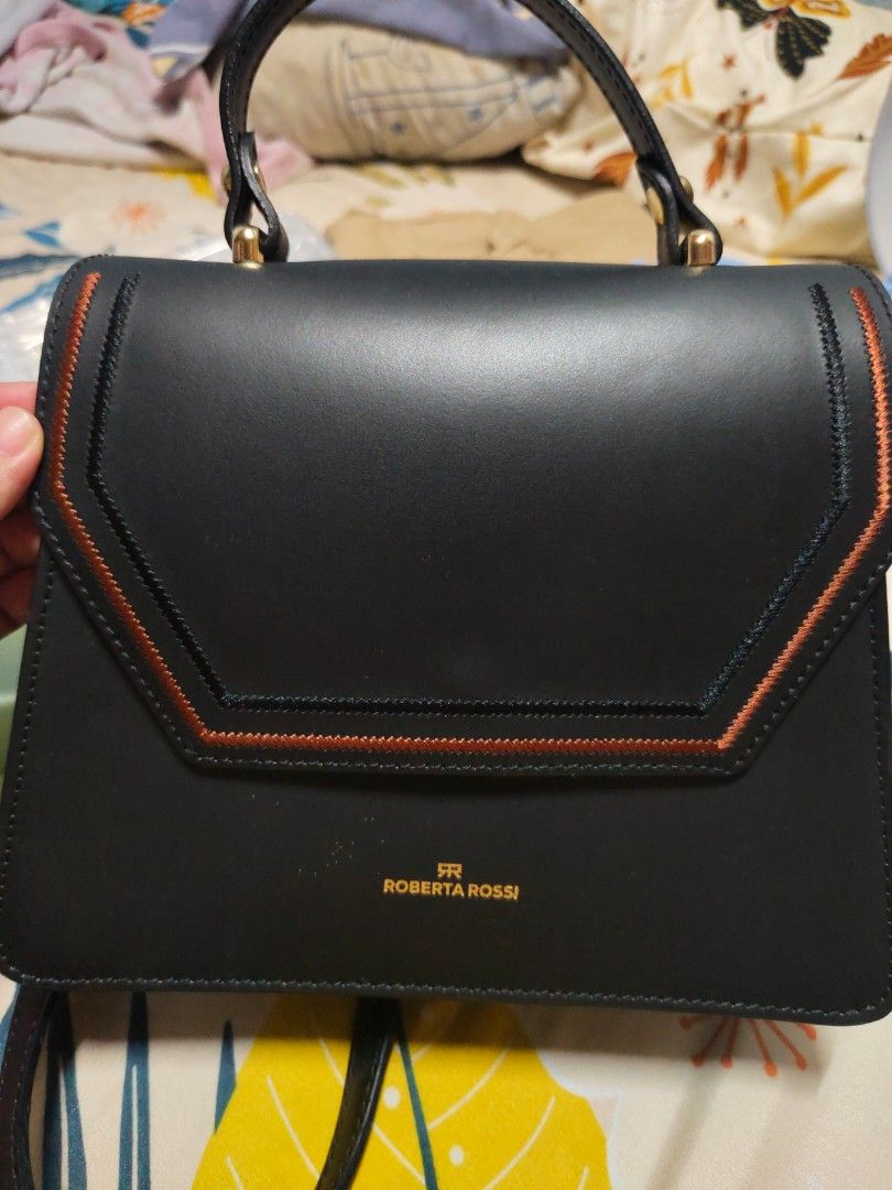 Roberta Rossi Black Leather Handbag (Category: Luxury Bags & Wallets) located in Manila. Submitted by swiftcloud_e4eddf (Listing ID 1466842630, Image 1). Description: - Brand: Roberta Rossi - Color: Black with chic contrast orange and dark stitching - Design: Structured flap-front handbag with sleek profile and clean lines - Hardware: Premium gold-tone hardware with gold foil brand logo - Handle & Strap: Single top handle plus a matching detachab