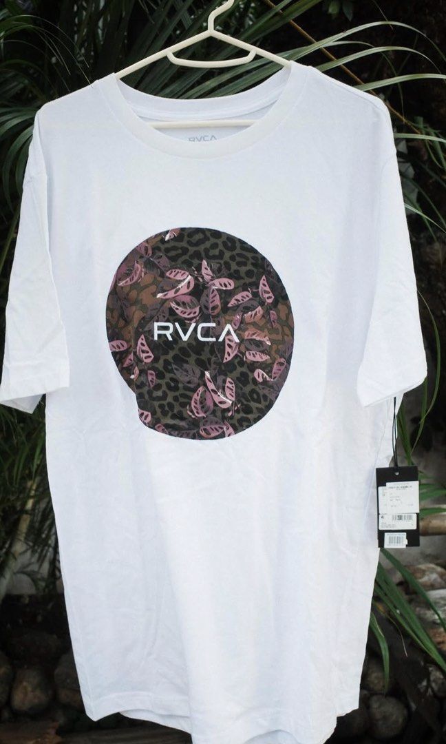 RVCA Purple Leaves White T-Shirt Medium (Category: Tshirts & Polo Shirts ) located in Cebu City. Submitted by declutterbarbie_ (Listing ID 1466833236, Image 1). Description: - Brand: RVCA - Size: Medium - Color: White - Condition: Brand new with tag attached on the sleeve - Design: Round chest graphic with purple leaves and leopard print, featuring RVCA text across the middle - Material: Soft cotton - Fit: Standard fit - Perfect for casual everyd